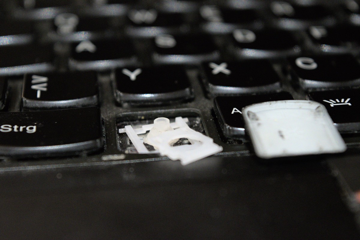 A laptop keyboard. The windows key has disintegrated, the keycap is lying beside flipped on its top side and the scissor mechanic that stabilizes the key is in pieces.